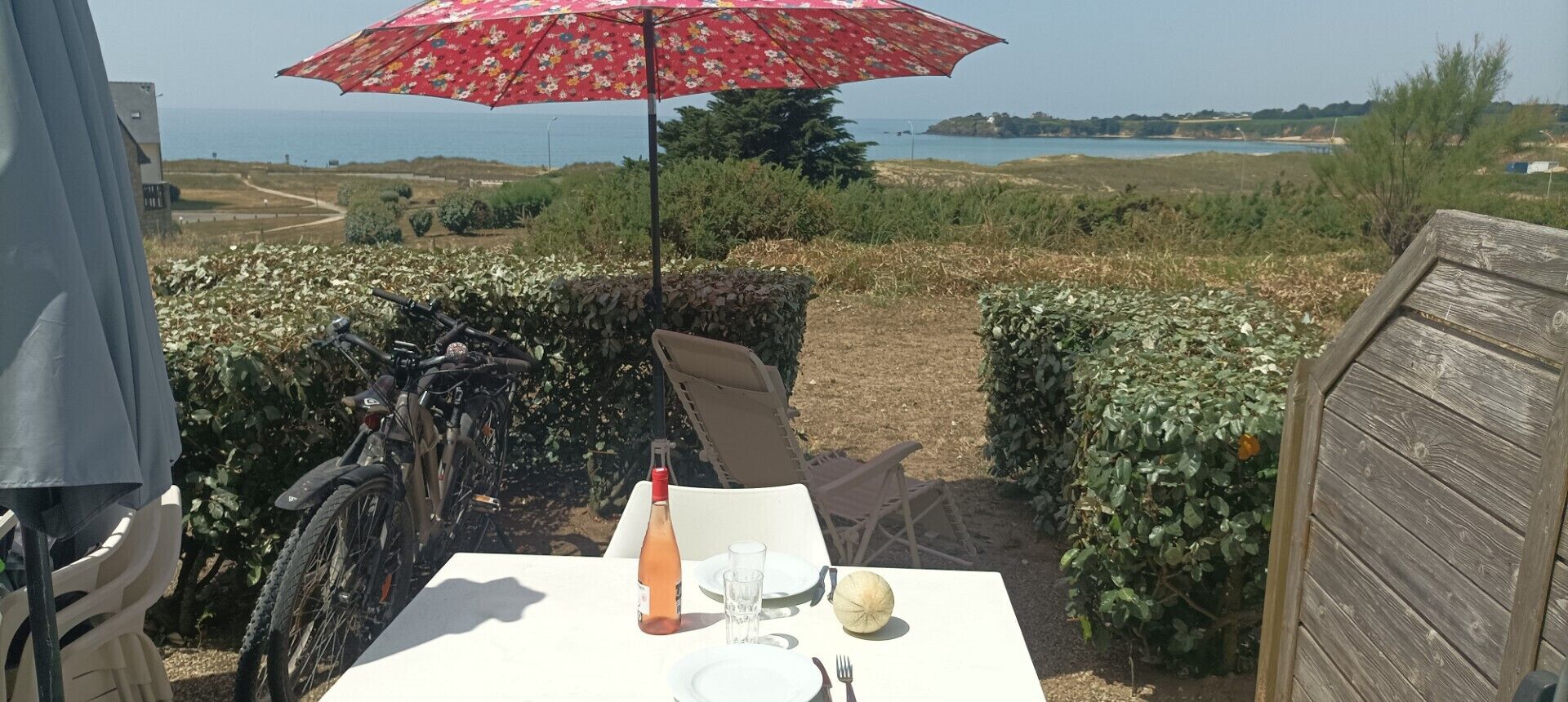 Une table avec une bouteille et un verre, un parapluie rouge et une vue sur la mer.