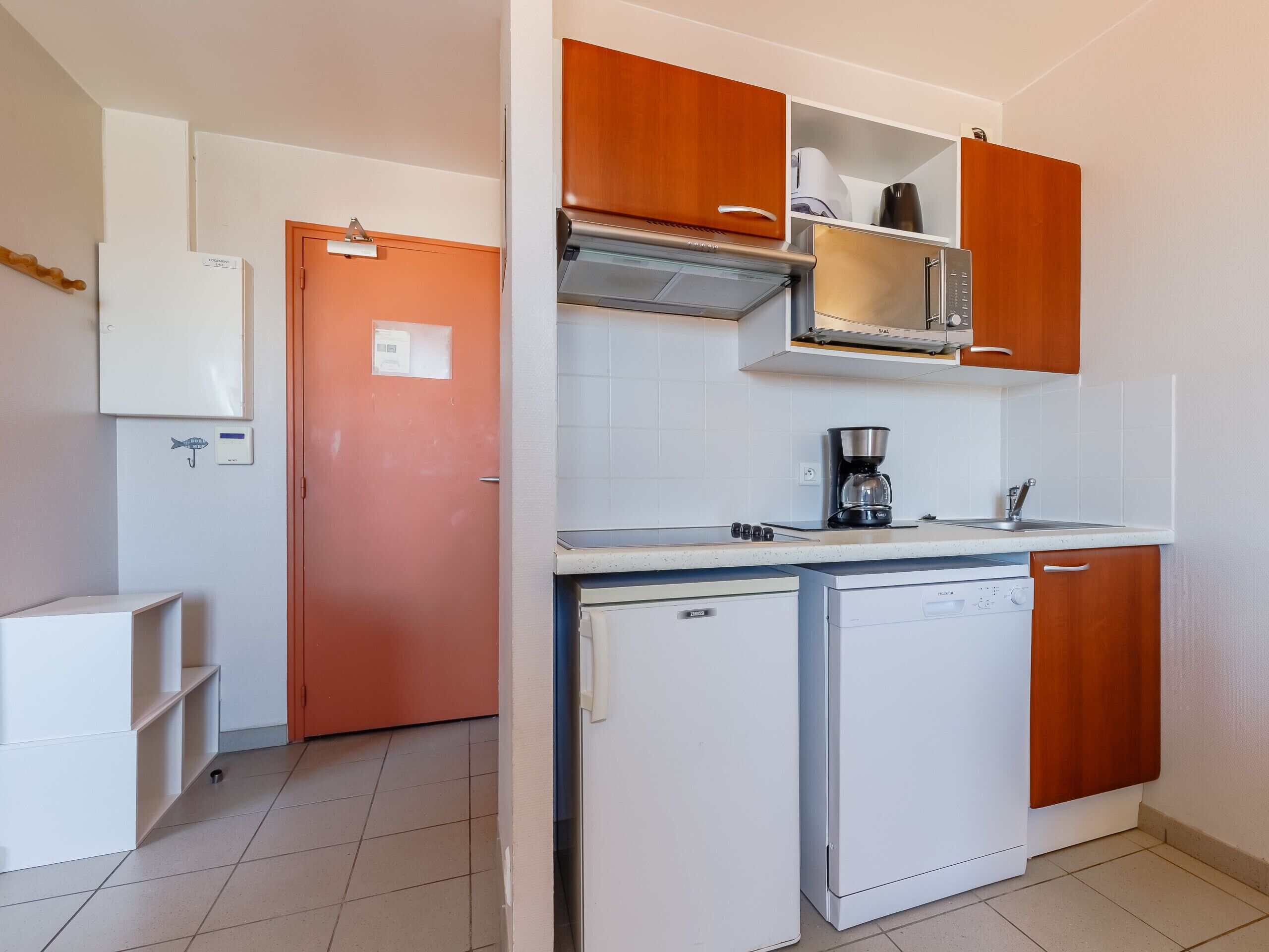 A compact kitchen with white appliances, wooden cabinets, and a tiled backsplash.