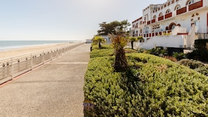 A coastal walkway with a beach view, a white building with red accents, and lush greenery. - Nice Apt 5 pers near the beach with pool (La Tranche-sur-Mer)