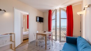 Ein Hotelzimmer mit Bett, Fernseher, Esstisch mit Stühlen, einer Couch und einem Balkon mit roten Vorhängen.