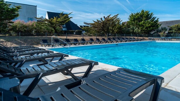 A swimming pool with lounge chairs, clear blue sky, and surrounding greenery.