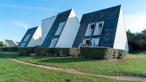 A row of modern, triangular-shaped houses with white and dark blue exteriors, arranged in a row with a well-maintained lawn and hedges in front.