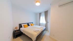 Een slaapkamer met een bed, nachtkastje, lamp en een airconditioner.