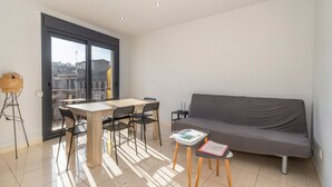 Un salon moderne comprenant un canapé, une table à manger avec des chaises, une petite table d’appoint et une grande fenêtre.