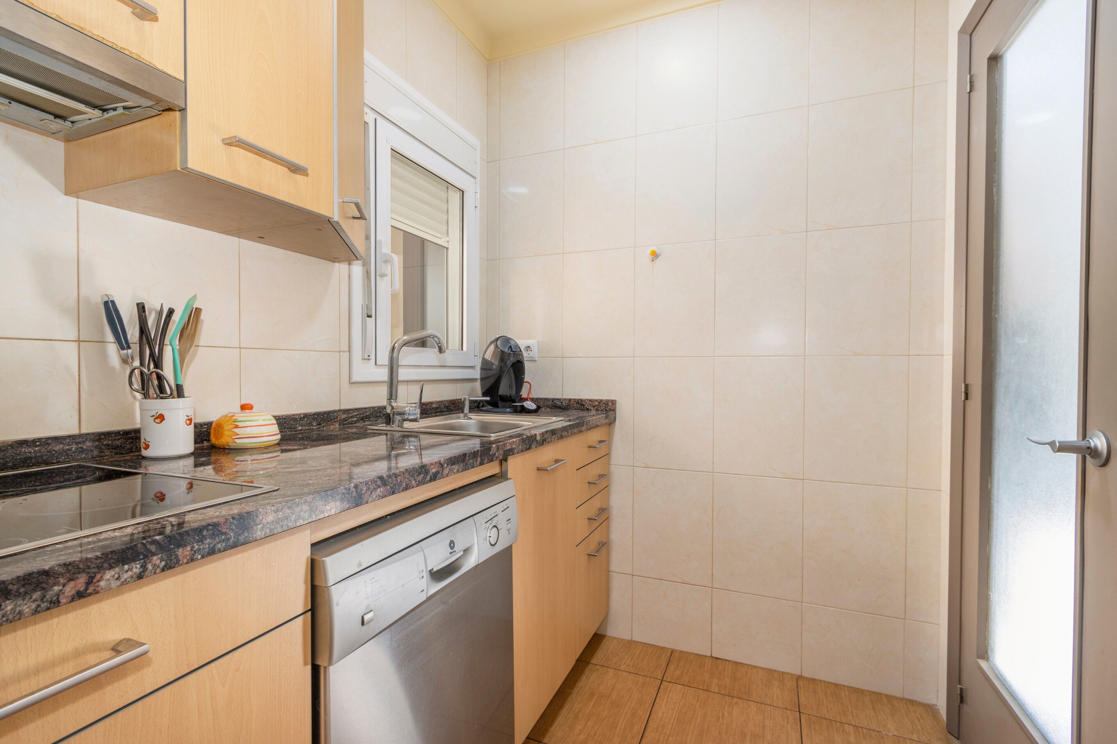 A kitchen with a dishwasher, a sink, and a window above the sink.