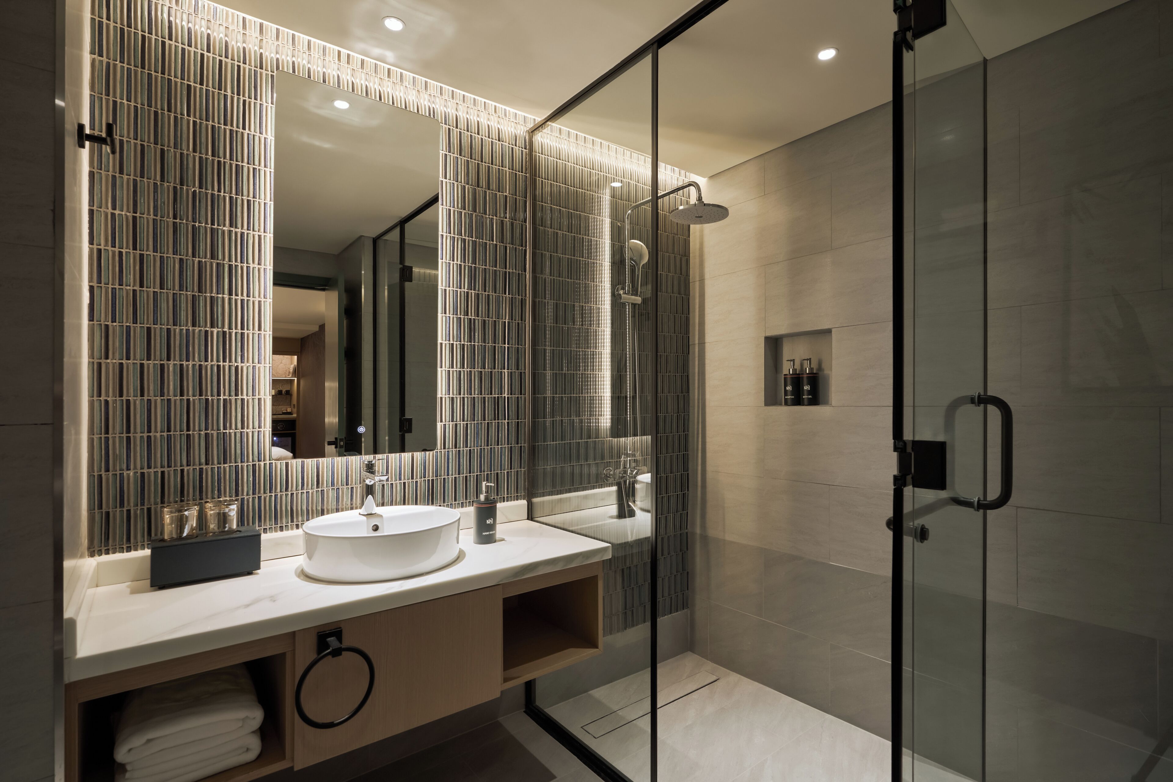Un baño moderno con ducha envuelta en vidrio, un espejo grande y un lavabo blanco.