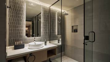 Un baño moderno con ducha envuelta en vidrio, un espejo grande y un lavabo blanco.