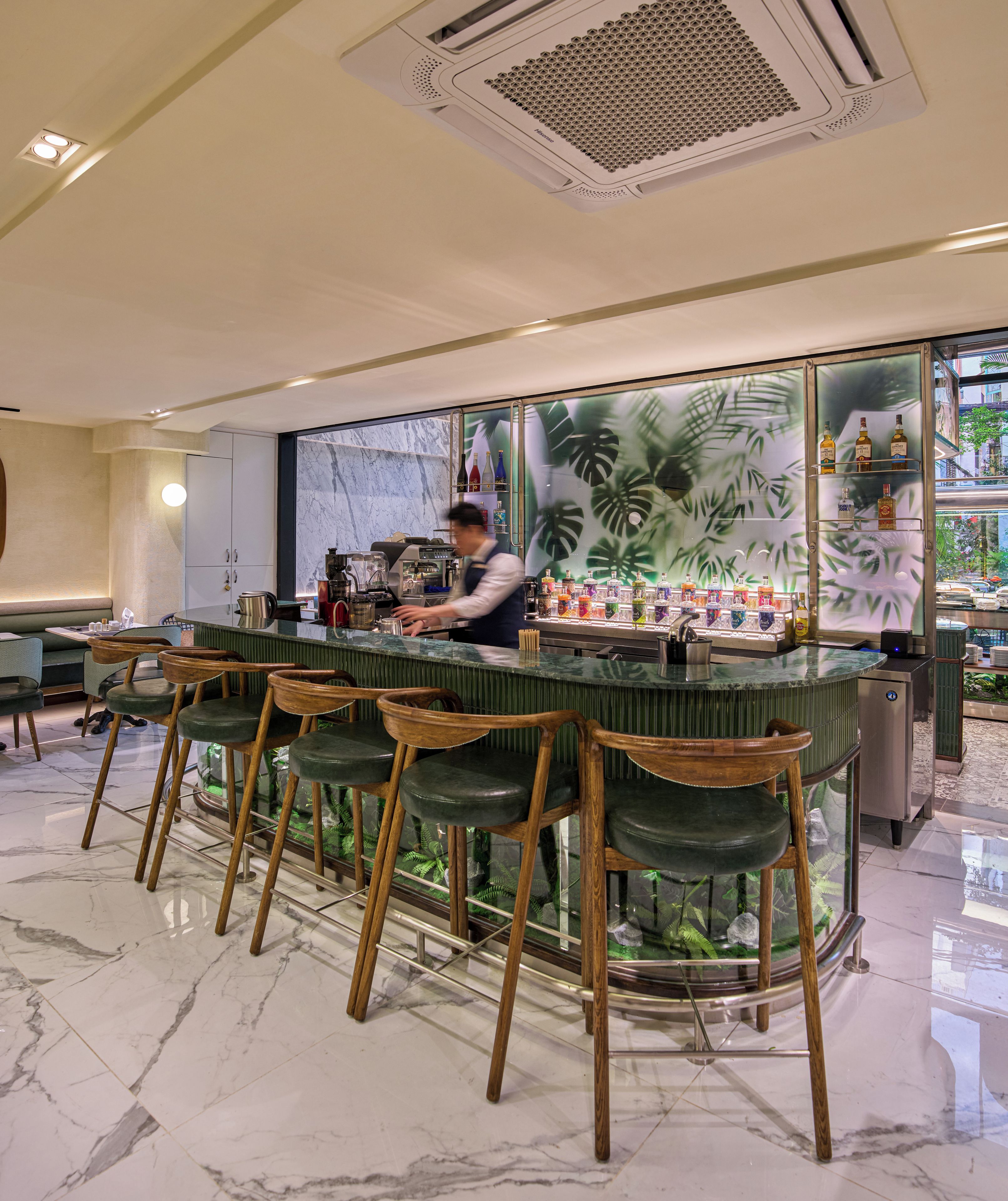 A bar area with a bartender, bar stools, a marble floor, and a tropical-themed wall.