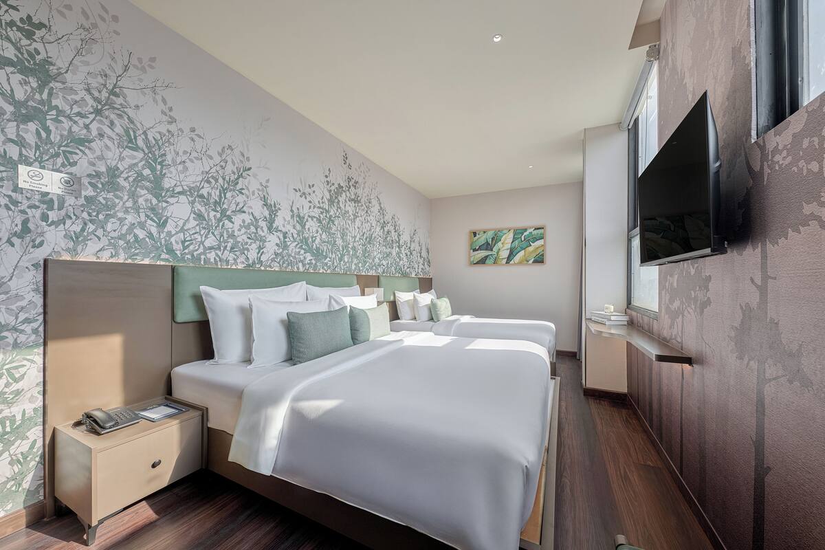 A hotel room with a large bed, a bedside table with a phone, a TV mounted on the wall, and a mural on the wall.