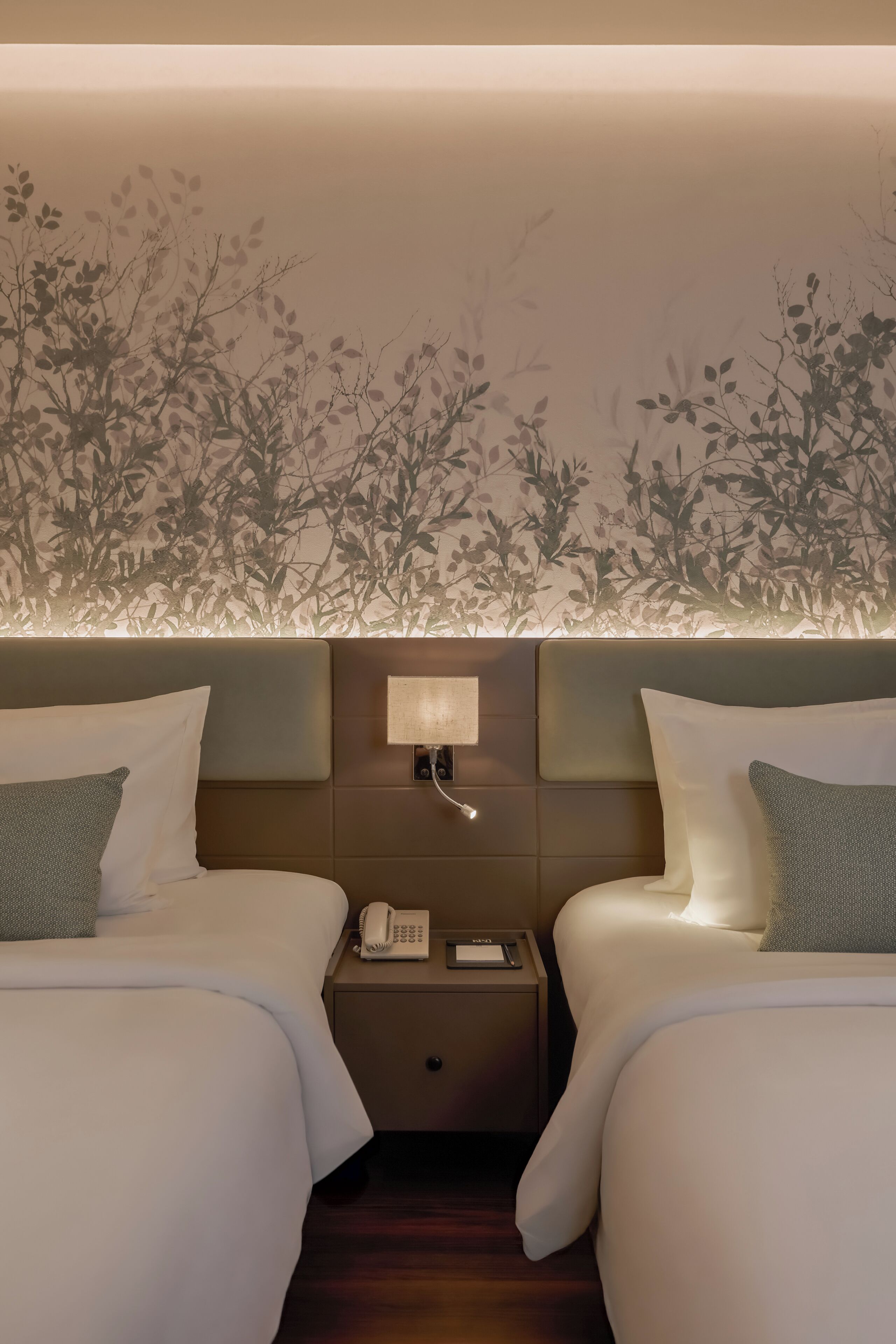A hotel room with two beds, a nightstand with a phone, and a wall with a leaf pattern.
