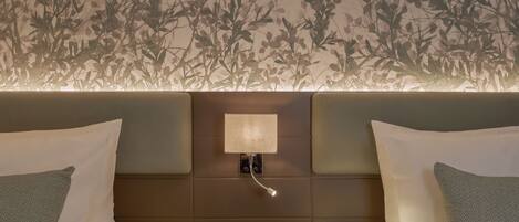 A hotel room with two beds, a nightstand with a phone, and a wall with a leaf pattern.