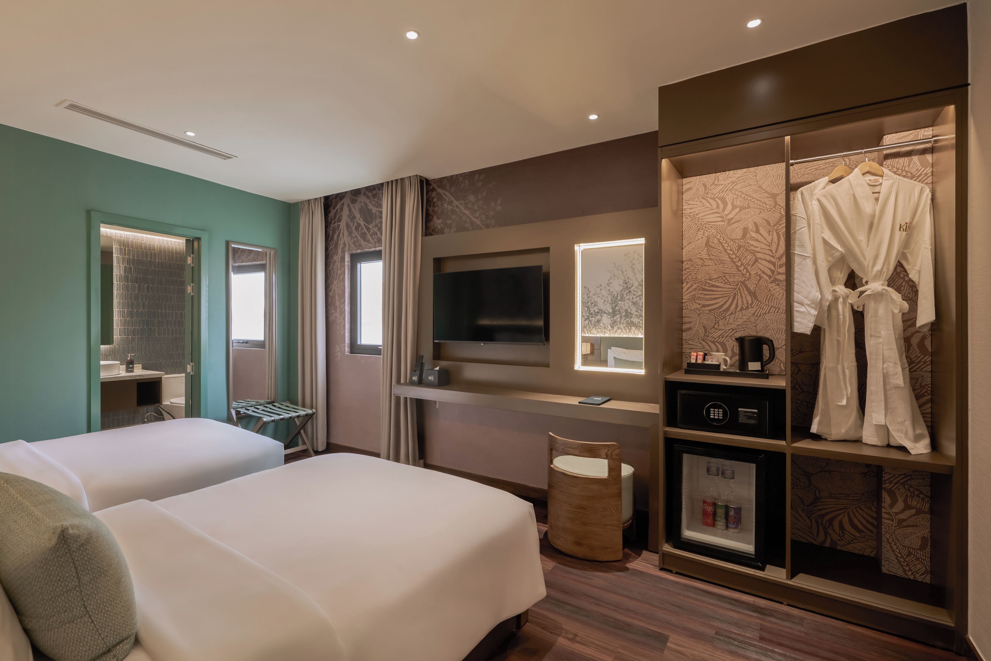 A hotel room with two beds, a TV, a minibar, and a robe hanging on a rack.
