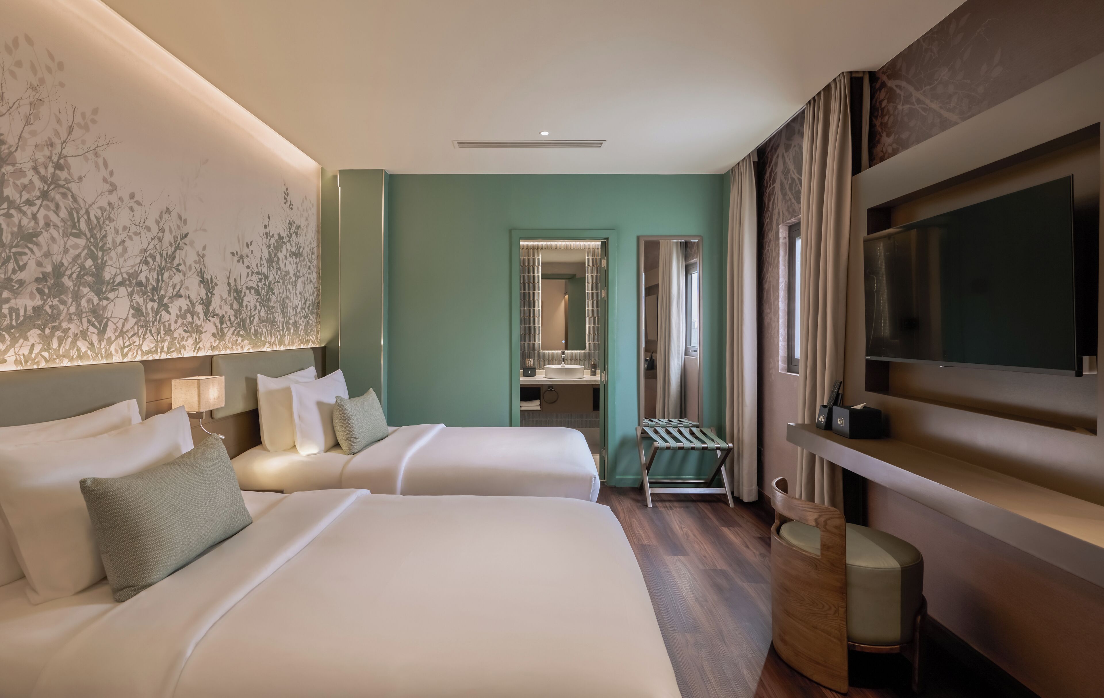Une chambre d’hôtel avec deux lits, une télévision, un bureau et une salle de bain visible à travers une porte ouverte.