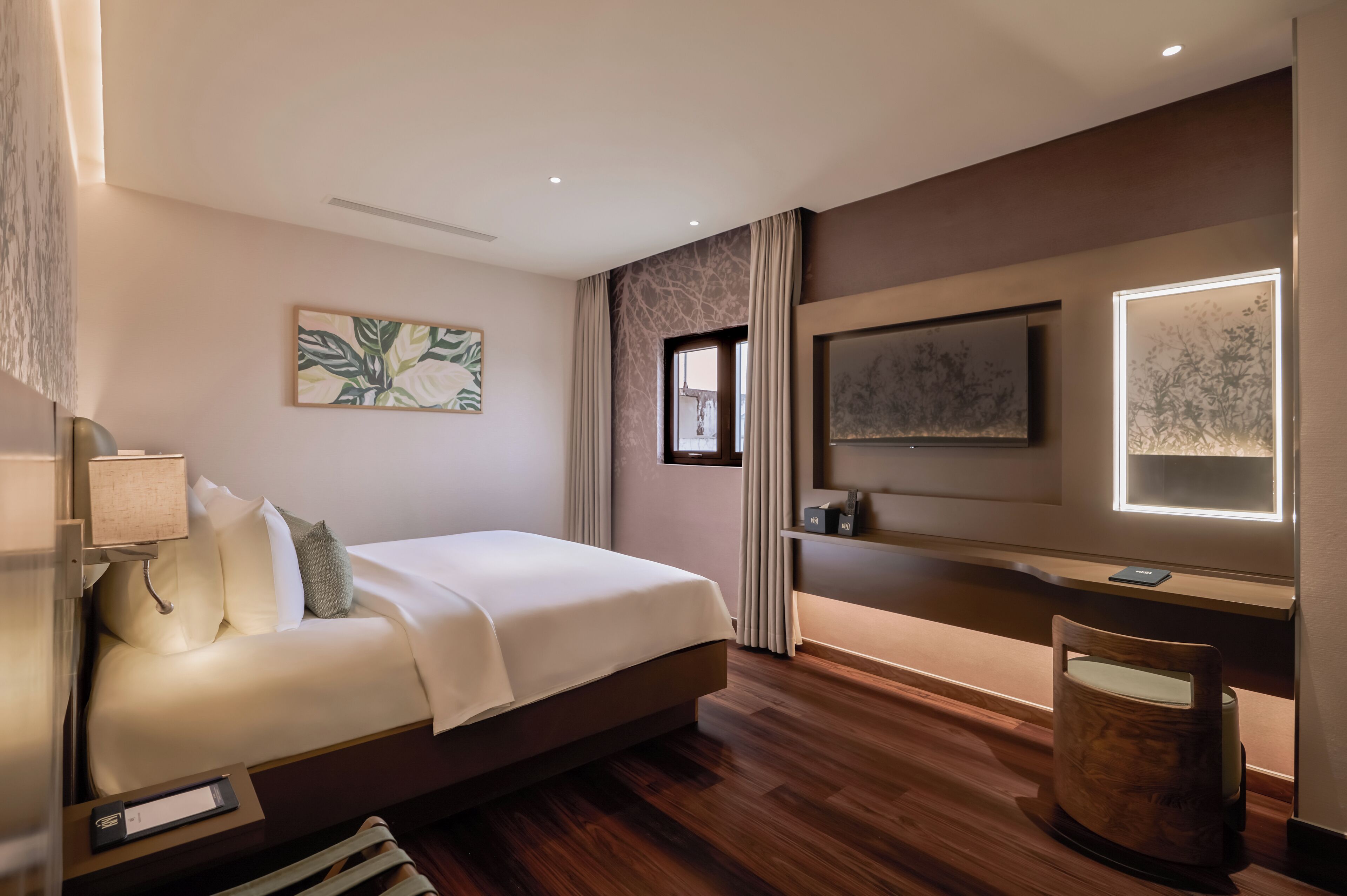 A modern hotel room with a large bed, a flat-screen TV, a bedside table, and a wooden nightstand.