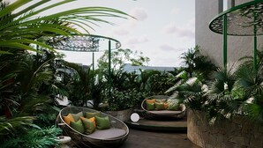 A modern outdoor seating area with wicker chairs and cushions, surrounded by lush greenery and a stone wall. - KiN Hotel Central Park (Ho Chi Minh City)