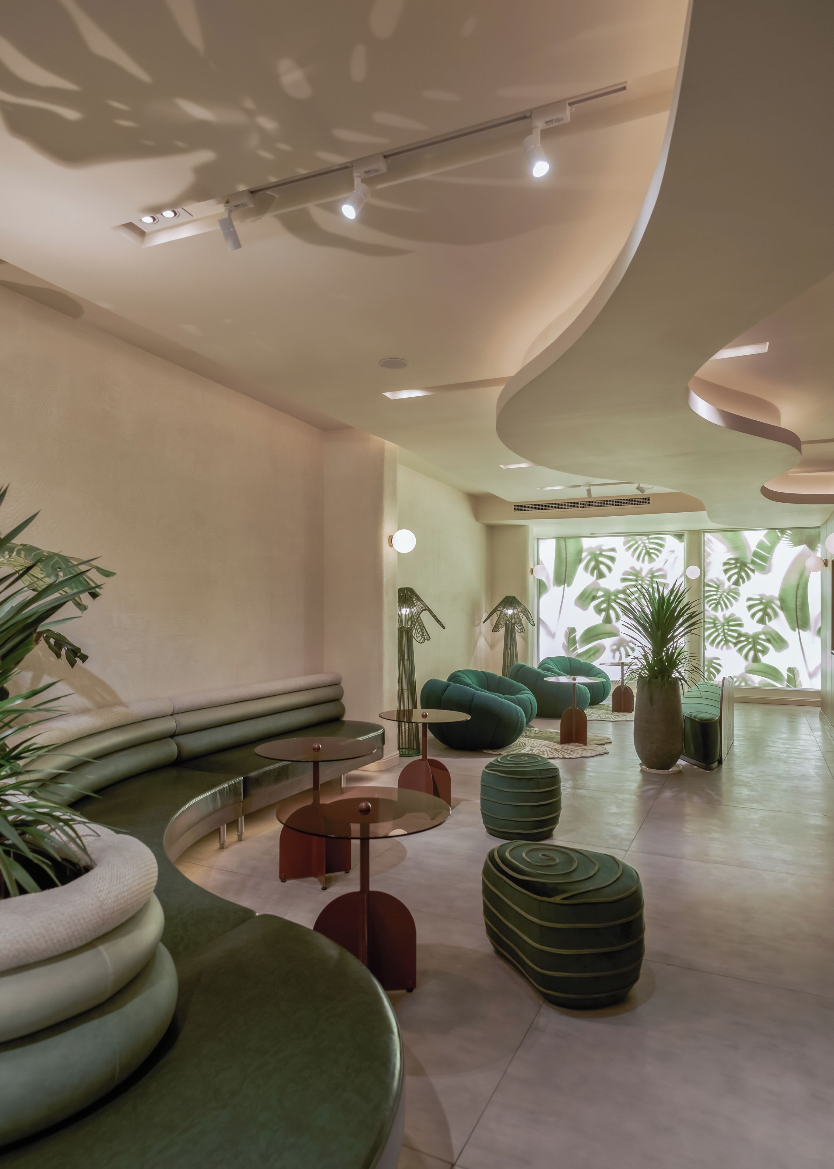 A modern interior with a curved ceiling, recessed lighting, and a seating area with green sofas and round tables.