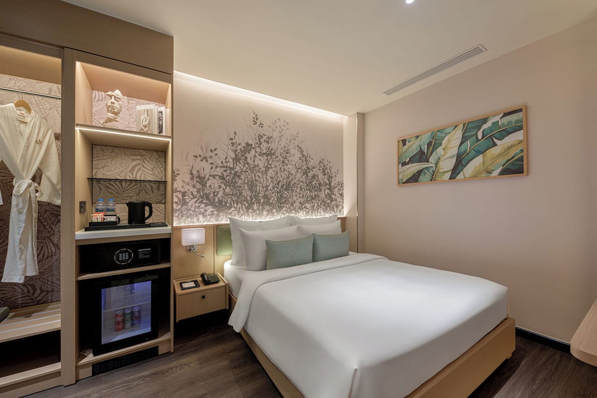 A hotel room with a bed, a vanity with a mirror, a shelf with toiletries, and a wall-mounted artwork.