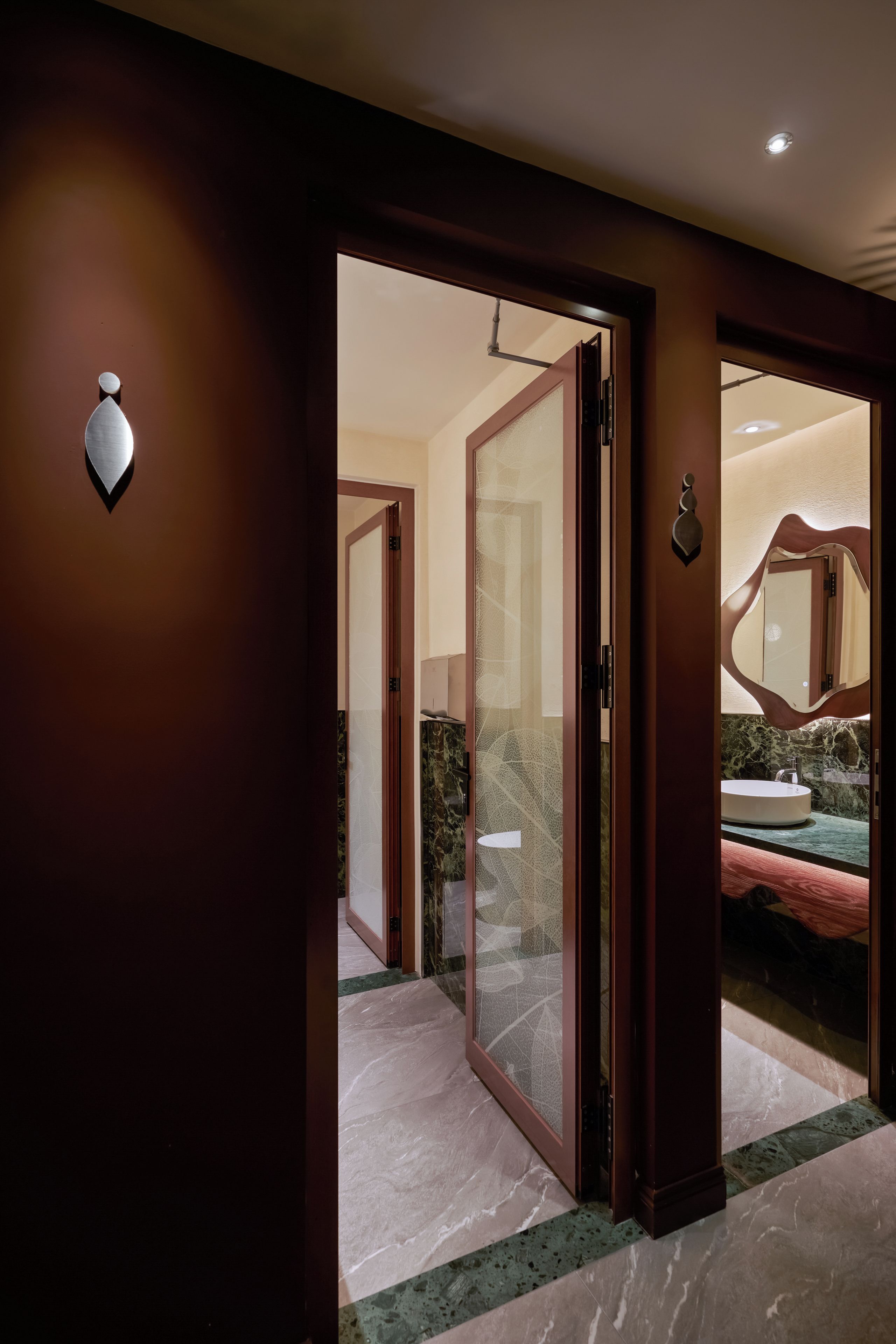 Une chambre d’hôtel avec un sol en marbre, une salle de bain avec un lavabo et un miroir, et une porte donnant sur une autre pièce.