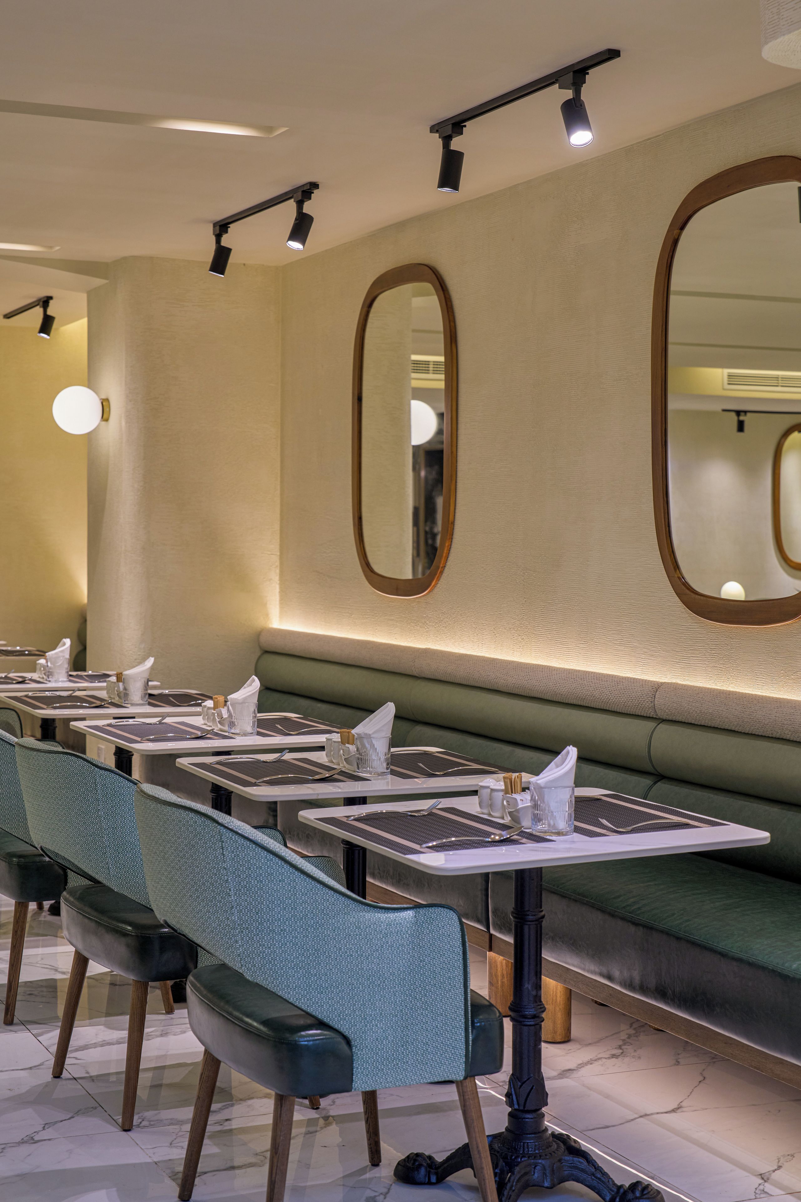 A restaurant interior with multiple tables and chairs, a green cushioned bench, and wall-mounted mirrors.
