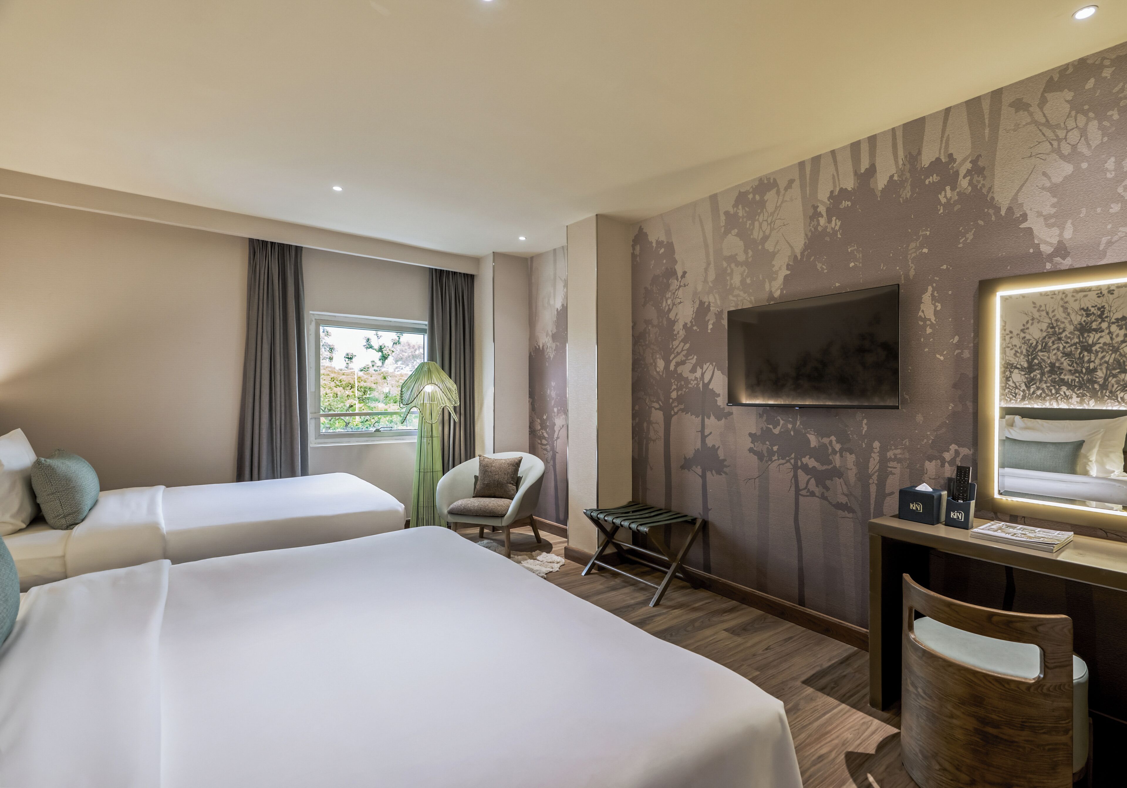 A hotel room with two beds, a desk with a TV, a chair, and a window with curtains.