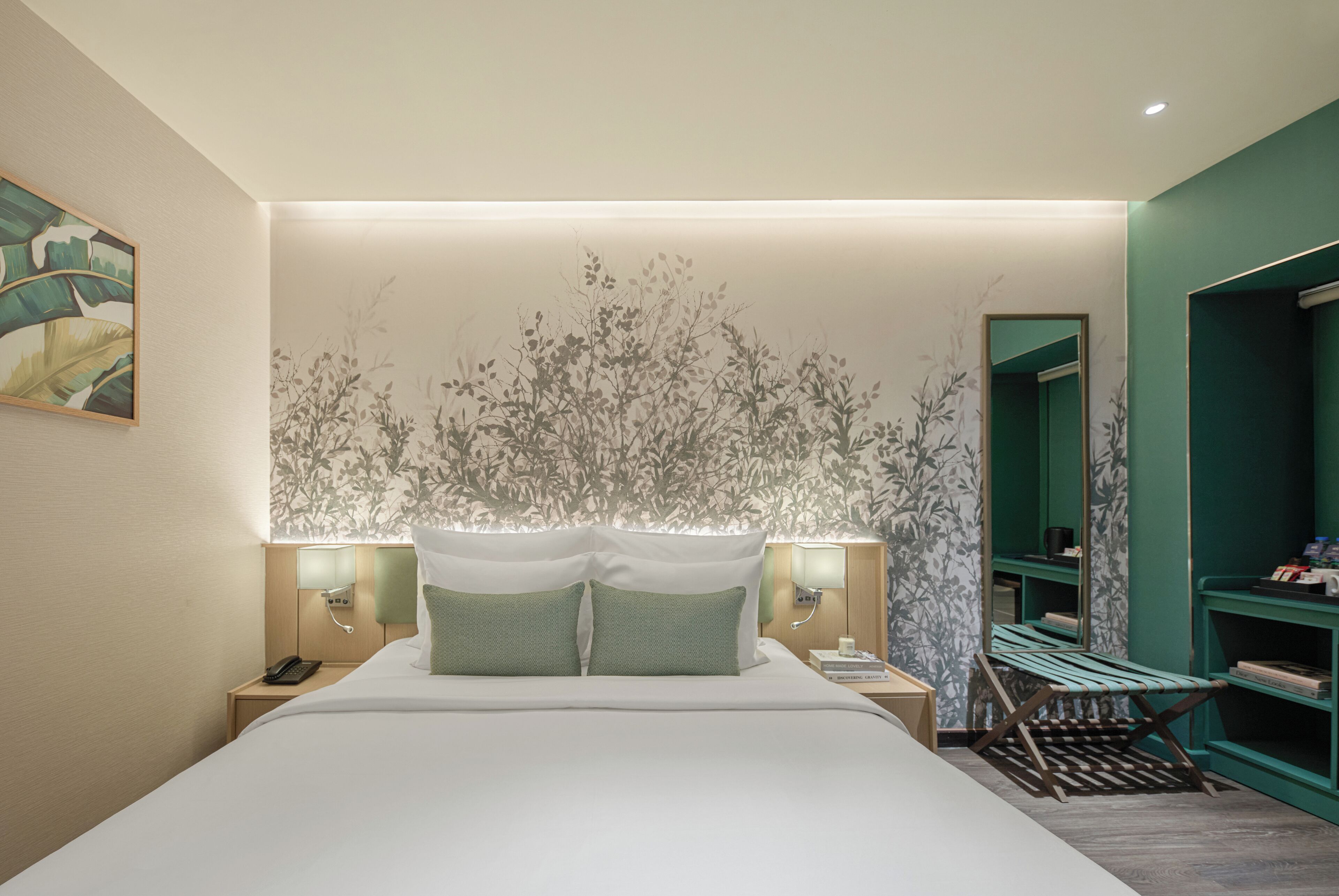 Een moderne hotelkamer met een groot bed, twee nachtkastjes, een bankje en een groene wand met een spiegel.