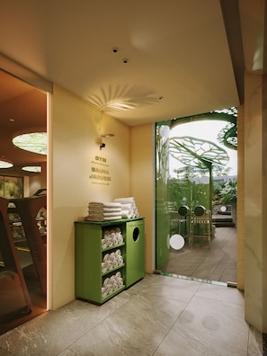 A hallway with a green towel rack, a wall-mounted sign, and a glass door leading to an outdoor area. - KiN Hotel Central Park (Ho Chi Minh City)