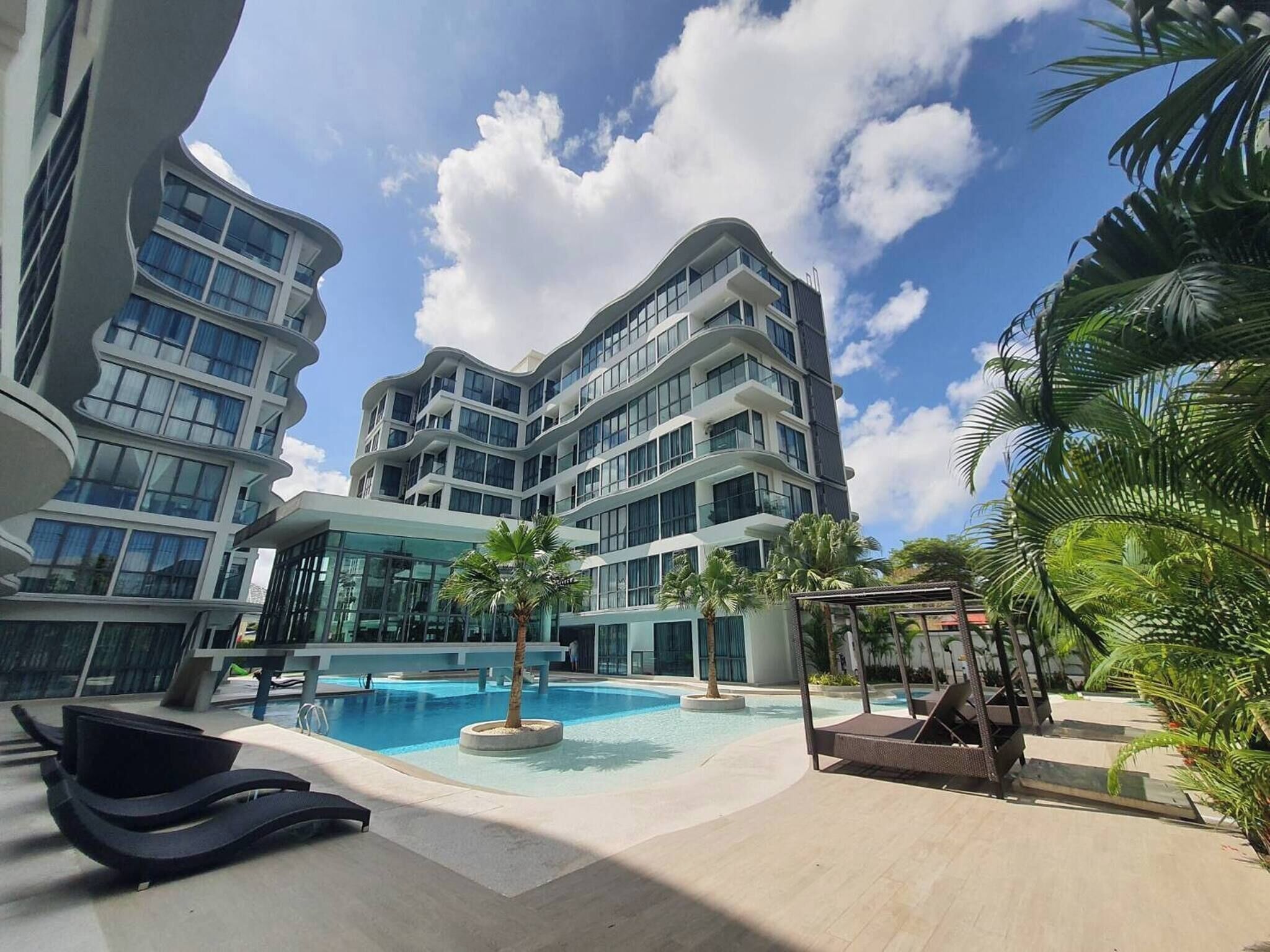 A modern hotel with a swimming pool, lounge chairs, and palm trees.