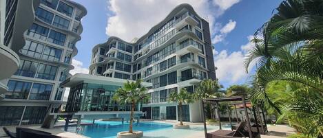 A modern hotel with a swimming pool, lounge chairs, and palm trees.