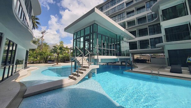 A modern hotel with a central swimming pool, multiple balconies, and a clear sky. - Stylish Bang Saray Apartment With Pool and Resort Facilities (Sattahip)