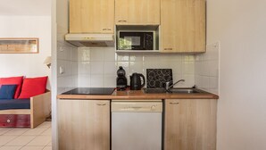 Una cocina compacta con armarios de madera, microondas, cafetera y lavavajillas.