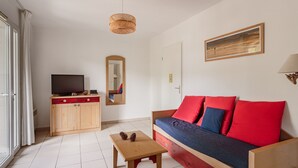 Una habitación con un sofá de madera, un televisor sobre un mueble de madera, una mesita pequeña de madera y una lámpara colgante.