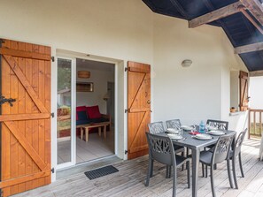 Une terrasse en bois avec une table dressée pour le repas, un canapé avec des coussins rouges et une porte donnant sur un espace abrité.
