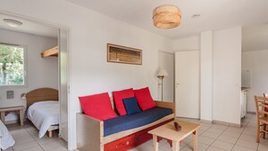 Una habitación con sofá de madera con cojines rojos y azules, una mesita de madera y una lámpara de techo tejida.