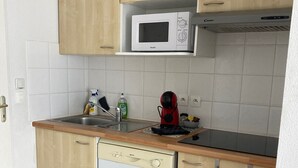 A compact kitchen with wooden cabinets, a white microwave, a dishwasher, and a sink. - apartment, balcony, view of nature, sleeps 6 (Ondres)