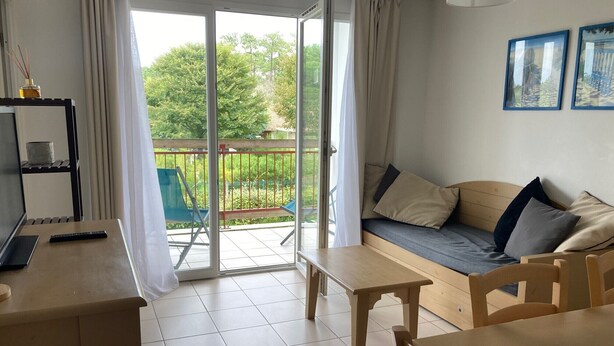 A cozy room with a sofa, a table, and a chair. There is a sliding glass door leading to an outdoor area with a balcony. - apartment, balcony, view of nature, sleeps 6 (Ondres)