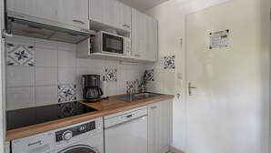 Una cucina compatta con mobili bianchi, un forno a microonde, una macchina per il caffè e una lavastoviglie.