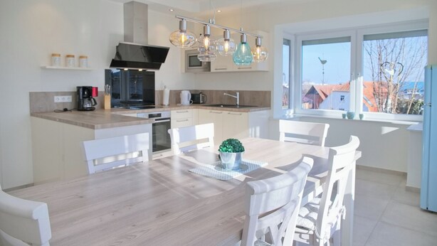 A modern kitchen with white cabinetry, a central island, and a dining area with white chairs. - Top modern vacation apartment 90 m² in a central location in Grömitz. (Grömitz)