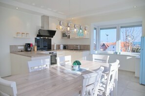 A modern kitchen with white cabinetry, a central island, and a dining area with white chairs. - Top modern vacation apartment 90 m² in a central location in Grömitz. (Grömitz)