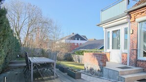 A patio with a wooden table and chairs, surrounded by potted plants and a brick wall. - Top modern vacation apartment 90 m² in a central location in Grömitz. (Grömitz)