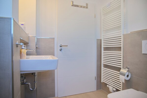A modern bathroom with a white sink, toilet, and radiator. - Top modern vacation apartment 90 m² in a central location in Grömitz. (Grömitz)