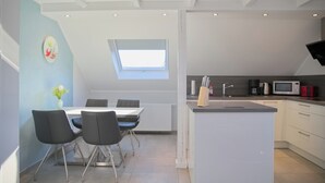 Ett modernt kök med en matplats, med en central köksö, vita skåp och ett takfönster ovanför matbordet.