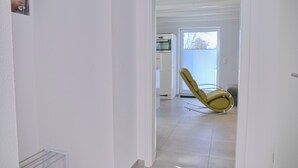 En hall med en gul gungstol, en vit dörr och ett köksområde i bakgrunden.