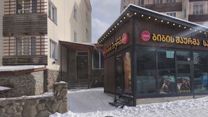 A restaurant with a stone facade and a wooden exterior, featuring a sign with foreign script and a contact number. - Snowy Loft Didveli (Bakuriani)