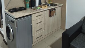 A compact kitchen with wooden cabinets, a built-in washing machine, a sink, and a countertop with various kitchen items. - Snowy Loft Didveli (Bakuriani)
