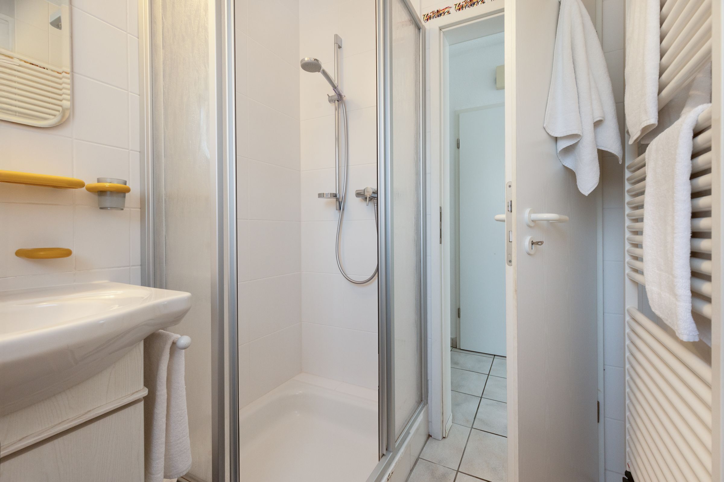 Een moderne badkamer met een douchecabine van glas, een wit wastafeltje en een handdoekrek.