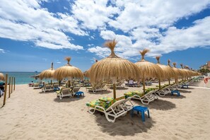 Ein Strand mit Reihen von Liegestühlen und Reetsonnenuren, einem klaren Himmel und dem Ozean im Hintergrund.