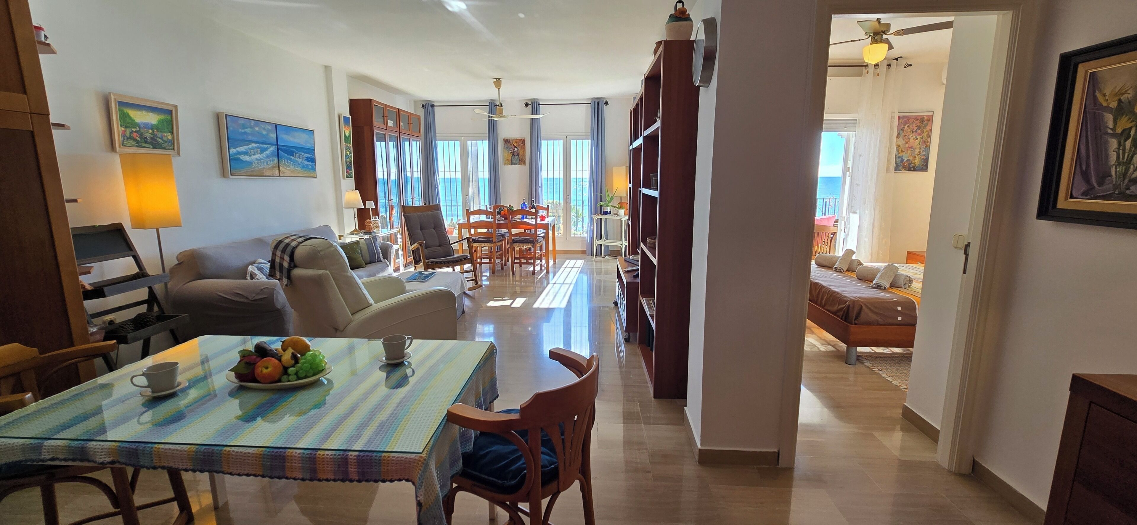 A spacious living area with a dining table set for two, a sofa, and a bookshelf.