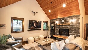 Una sala de estar moderna con chimenea, sofás de cuero, un televisor de pantalla plana y techo de madera.