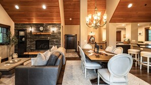Un amplio salón con chimenea, un comedor con una larga mesa y sillas blancas, y una cocina al fondo.
