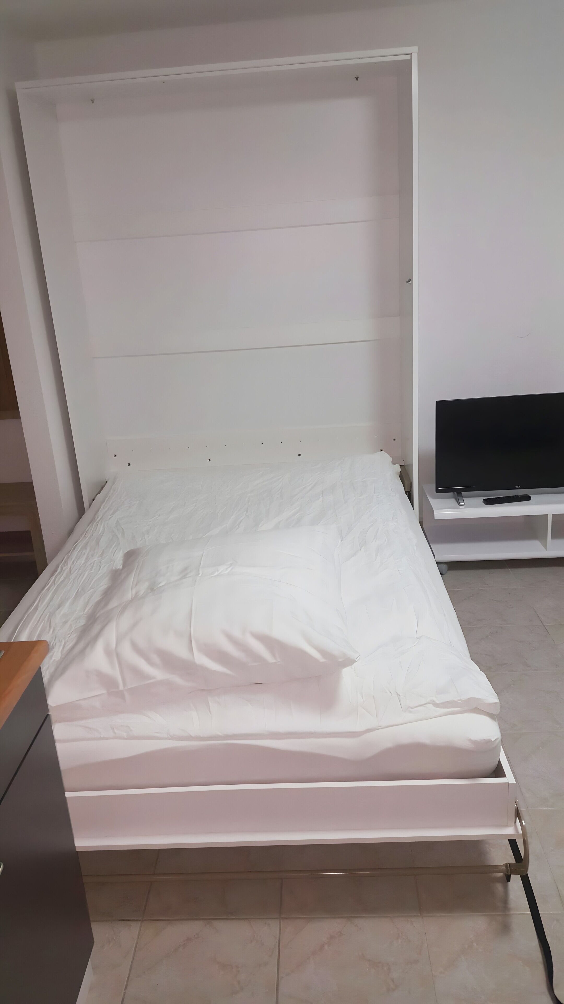 A bed with white bedding, a TV on a stand, and a wooden dresser.